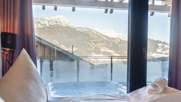 A hotel room with a bed, a hot tub, and a view of snow-covered mountains. - Superior 3 SZ Sauna & Aussenbadewanne by Interhome (Haus)