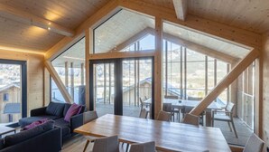 A spacious loft-style room with a large wooden dining table, comfortable seating, and expansive windows offering views of the surrounding area. - Superior 3 SZ Sauna & Aussenbadewanne by Interhome (Haus)