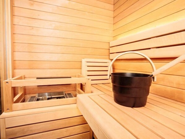 A wooden sauna with benches and a black bucket.