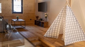 En inredning med träpanel och trägolv, en tv som är monterad på väggen, ett litet bord med en växt och en tipi-liknande konstruktion.