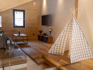 Een houten interieur met een houten vloer, een aan de muur bevestigde televisie, een klein tafeltje met een plant en een tipi-constructie.