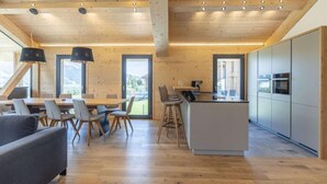 A modern interior with a wooden ceiling, a dining area with a table and chairs, a kitchen with a bar, and a sofa. - Premium mit 4 Schlafzimmern,Sauna&Pool by Interhome (Haus)