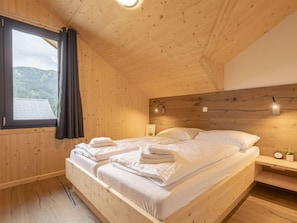 A wooden cabin bedroom with a bed, a nightstand, a wall-mounted light, and a window with curtains.