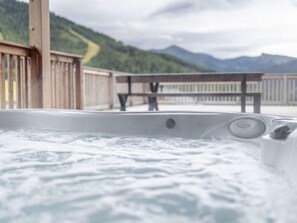 Uma banheira de hidromassagem com um deck de madeira e um banco, emoldurada por uma paisagem montanhosa.