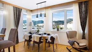 A dining area with a table set for four, wooden flooring, and a view of a snowy landscape through large windows.