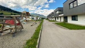 A modern building with a playground in front, a clear sky, and a road leading to it.