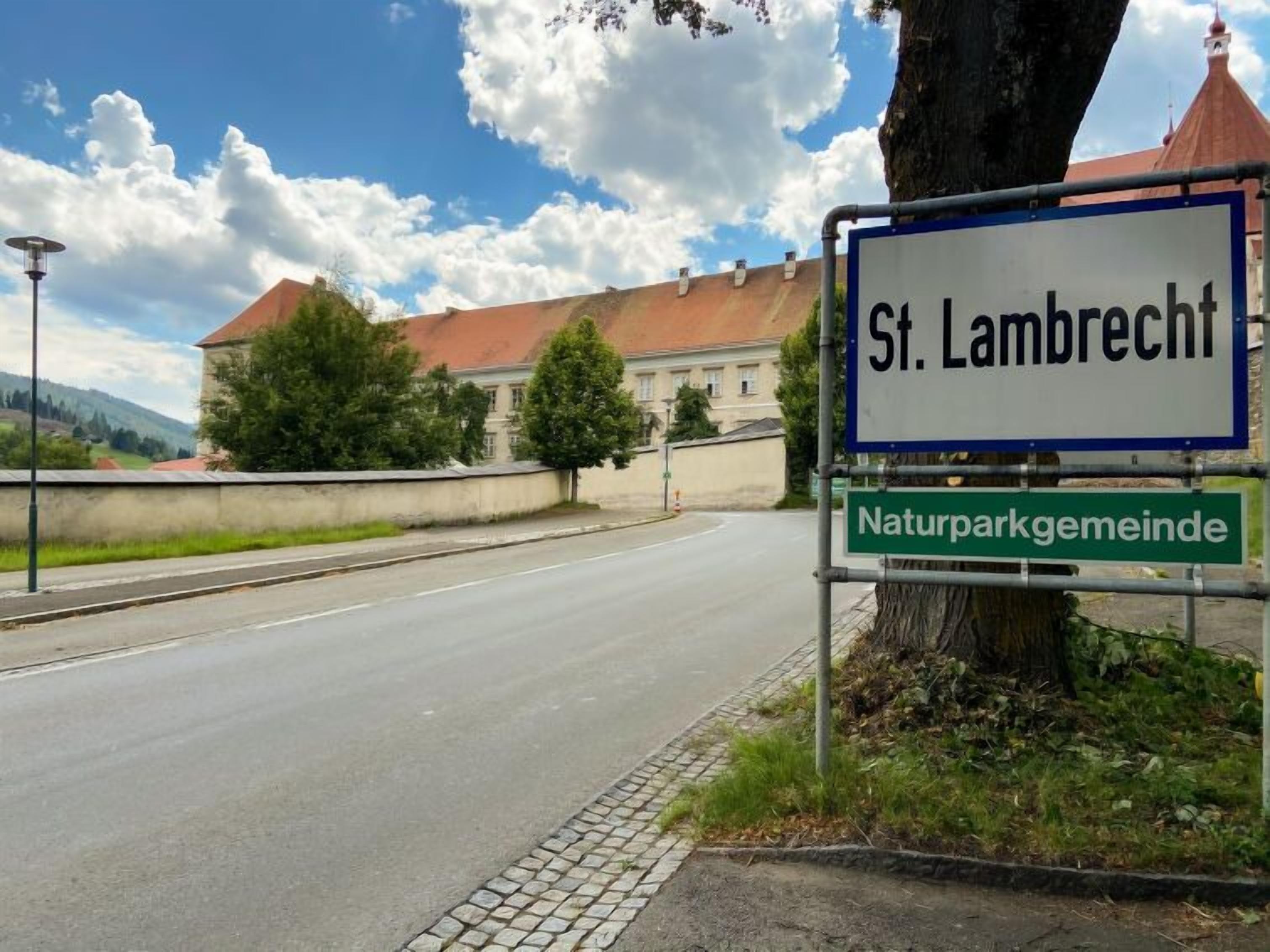 A road sign indicating 'St. Lambrecht' and 'Naturparkgemeinde' with a building in the background.