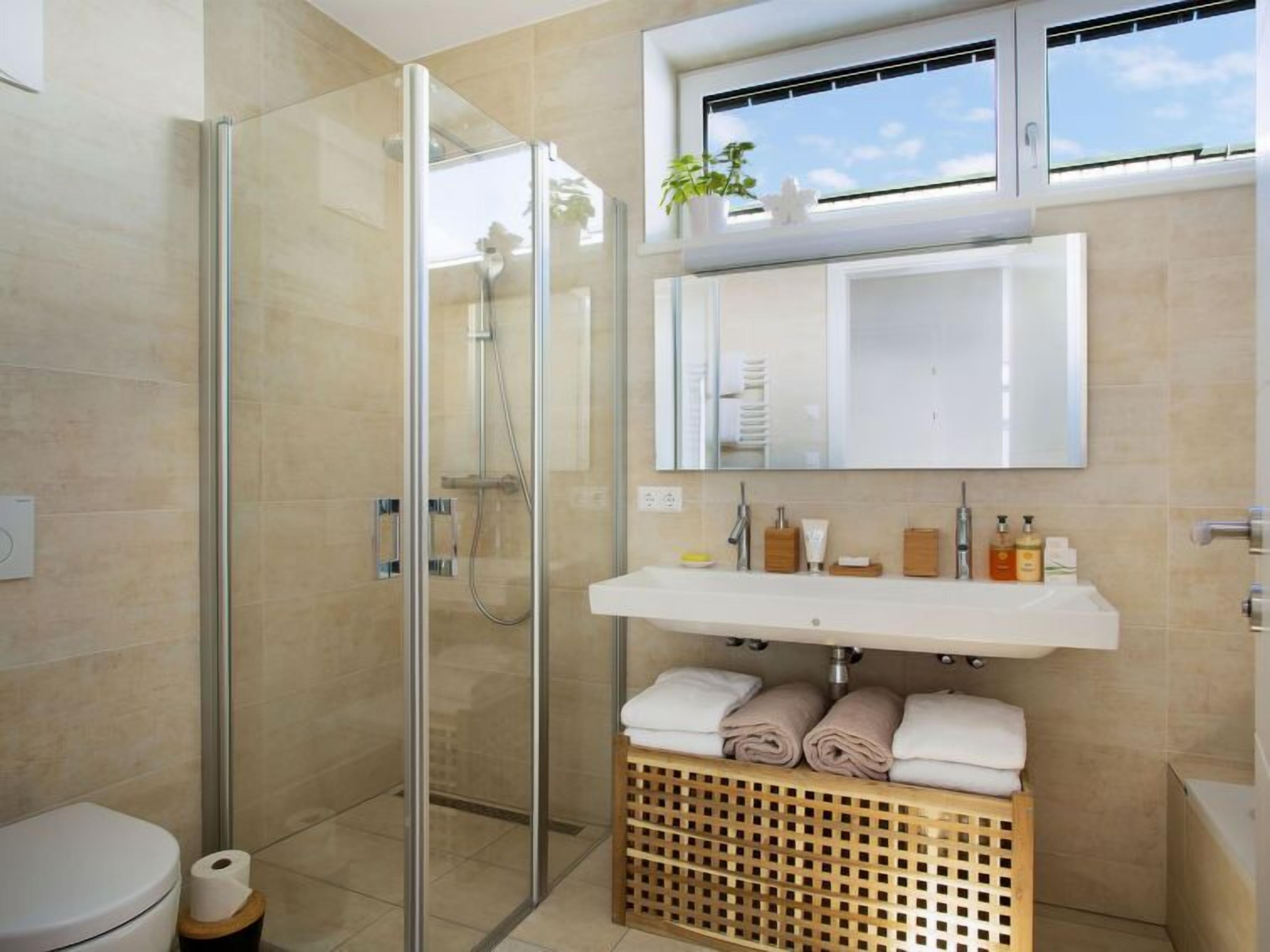 Ein modernes Badezimmer mit Duschkabine aus Glas, einem weißen Waschbecken und einem Wäschekorb aus Holz.