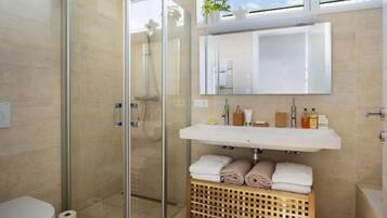 Ein modernes Badezimmer mit Duschkabine aus Glas, einem weißen Waschbecken und einem Wäschekorb aus Holz.