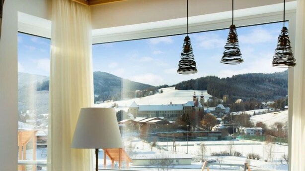 A room with a large window offering a view of a snowy village, a table set with dinnerware, and three hanging pendant lights.