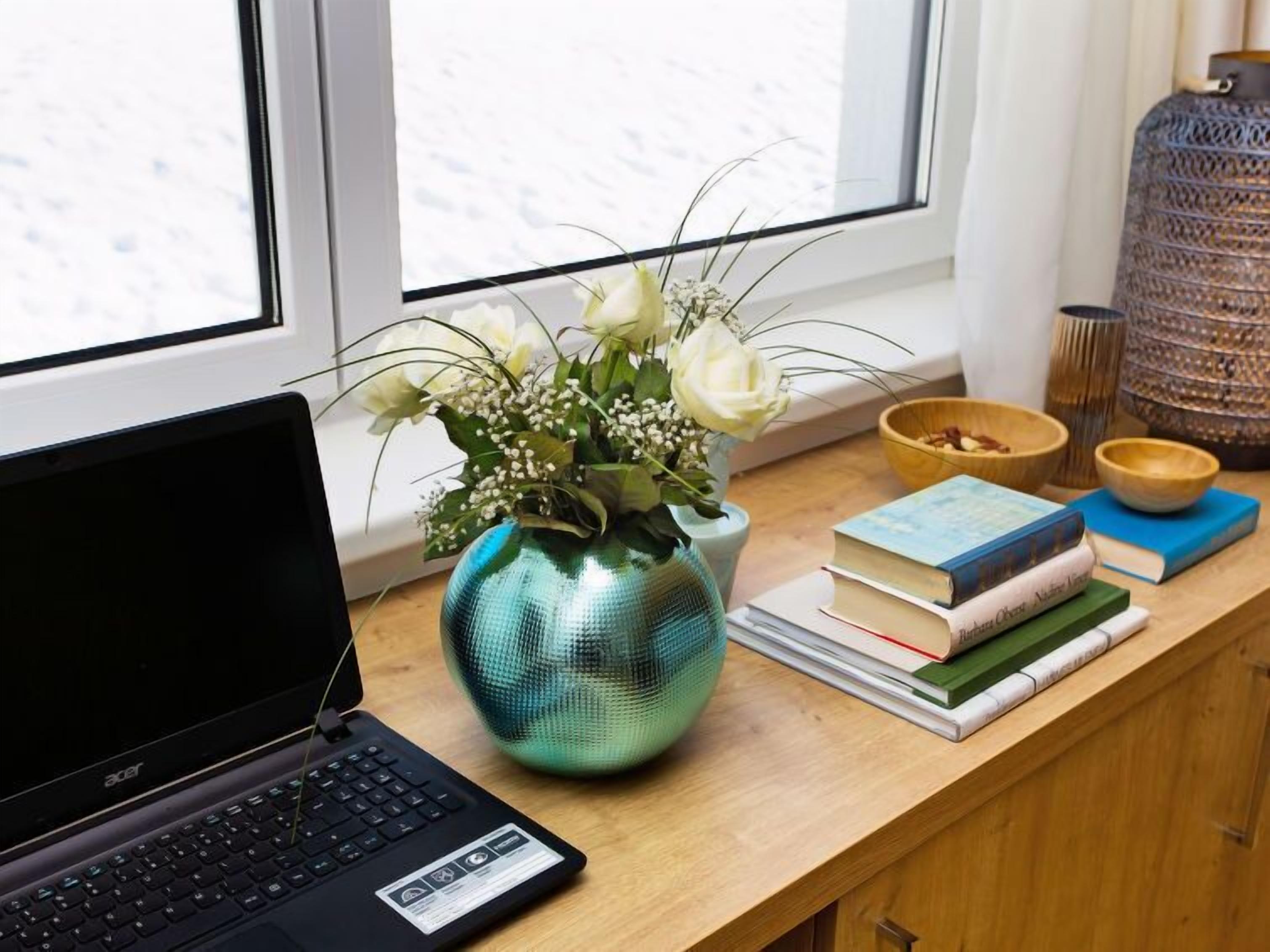 Un ordinateur portable posé sur un bureau en bois, avec un vase de fleurs, des livres et des bols décoratifs.
