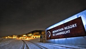 A sign for Mountain Resort St. Lambrecht with a modern building in the background.
