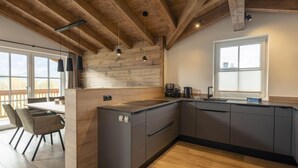 Une cuisine moderne avec des poutres en bois, un coin repas avec une table et des chaises, et une grande fenêtre offrant une vue dégagée.