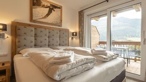 Ein Schlafzimmer mit einem großen Bett, einem hölzernen Kopfteil, einem Gemälde eines Skifahrers und einem Balkon mit Bergblick.