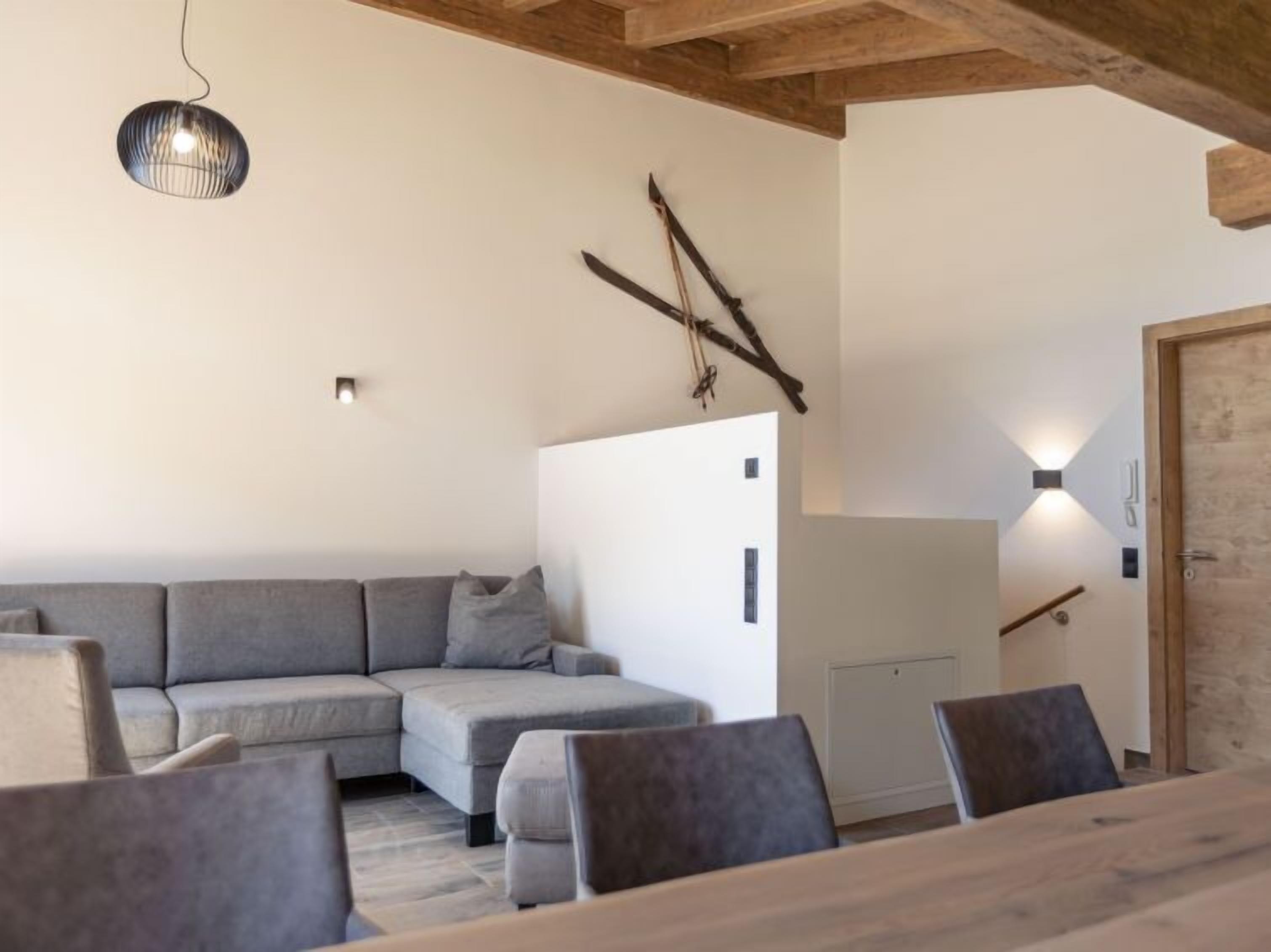 A modern living room with a grey sectional sofa, a wooden dining table with chairs, a hanging light fixture, and a wall-mounted light.
