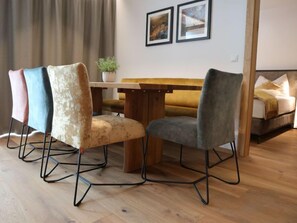 Een eethoek met een houten tafel en vier stoelen met metalen poten. Achtergrond toont een bank en een bed.
