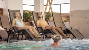 Zwei Personen entspannen in Liegestühlen am Pool, eine dritte Person befindet sich im Wasser.