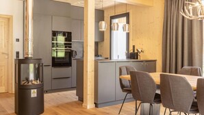 Een moderne keuken met een houtkachel, grijze kastjes en een eethoek met grijze stoelen.