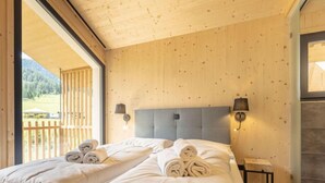 Een tweepersoonskamer met houten wanden en een groot raam. Er staan twee bedden met witte lakens en keurig opgevouwen handdoeken.