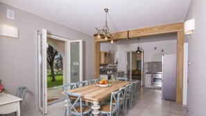 Uma sala de jantar espaçosa com uma mesa de madeira e cadeiras azuis, uma cozinha ao fundo e vista para o exterior.