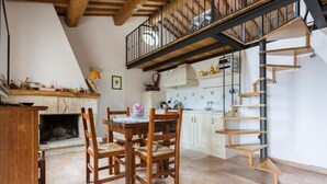 A rustic kitchen with a dining table, chairs, a fireplace, and a spiral staircase. - Rent house in the valley of Menotre (Pale)