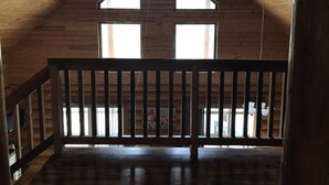 Un interior de madera con techo inclinado, dos ventanas y una barandilla de madera.