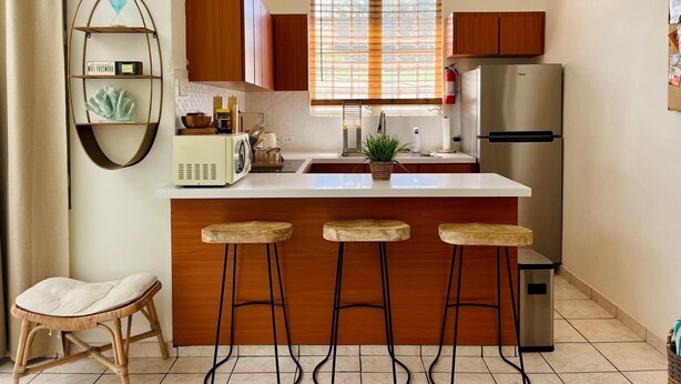 Uma cozinha moderna com armários de madeira, uma geladeira de aço inoxidável, forno embutido, cafeteira e um banquinho.