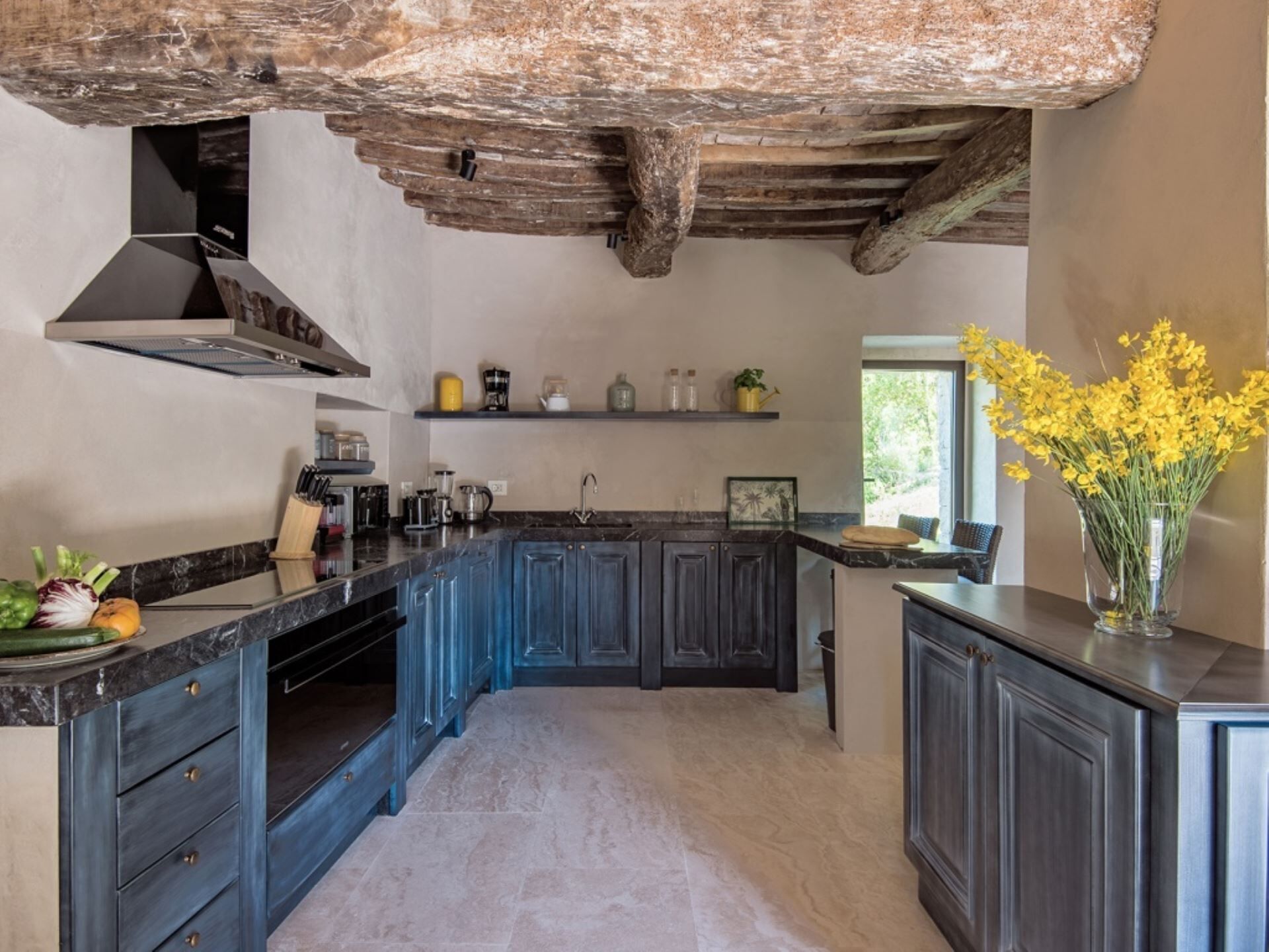 A kitchen with dark blue cabinets, a marble countertop, and a rustic ceiling.