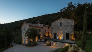 A stone house with a gravel driveway, surrounded by greenery and a hill in the background. - Luxury villa inside a splendid estate (Perugia)