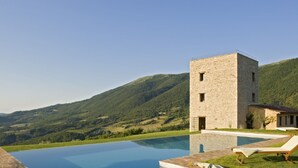 Un edificio de piedra con piscina y sillones de descanso.