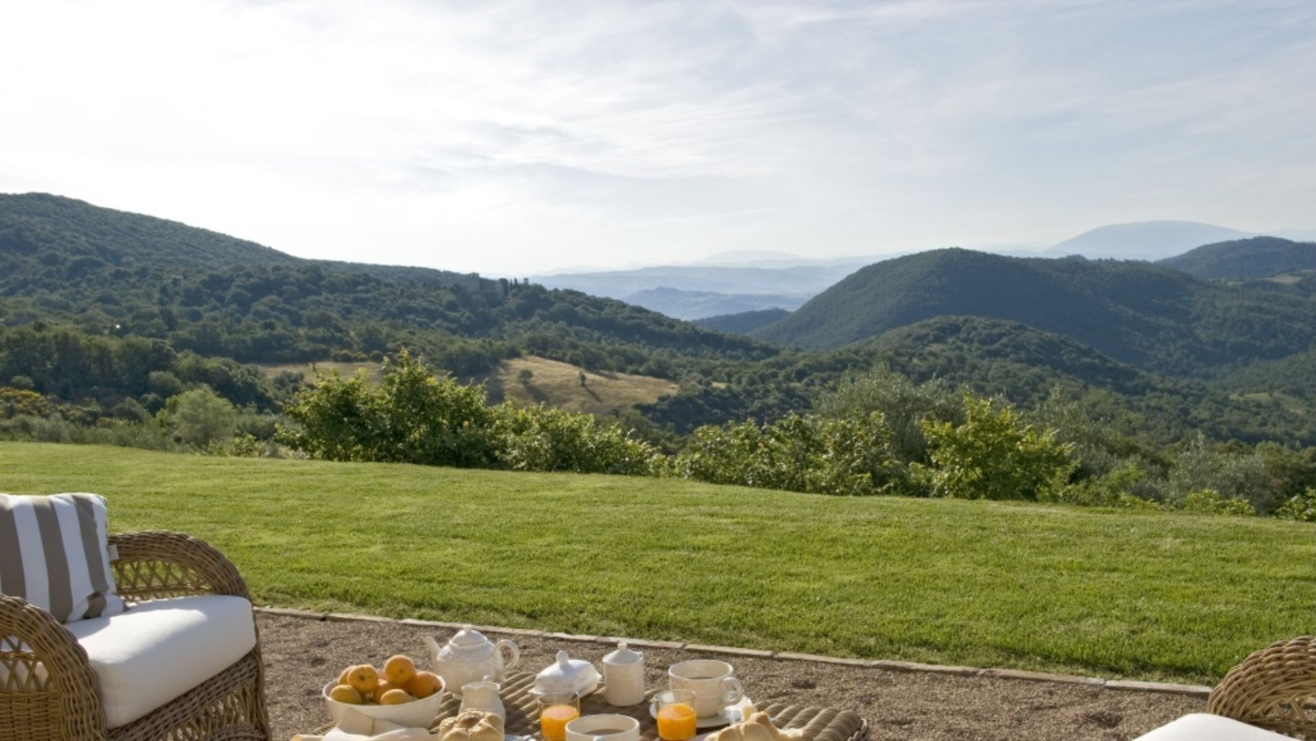 A dining area with a table set for breakfast, overlooking a valley with hills and trees.