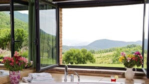 Ein Badezimmer mit großem Fenster und Blick auf eine grüne Landschaft und Berge.