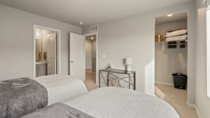 A bedroom with two beds, a desk, a chair, a closet, and a bathroom visible through an open door. - Trendy Townhome 20 minutes to Fort Collins, Greeley, and Windsor (Ault)