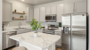 A modern kitchen with white cabinets, stainless steel appliances, and a marble countertop. - Trendy Townhome 20 minutes to Fort Collins, Greeley, and Windsor (Ault)