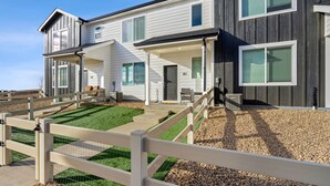 A two-story house with a front porch, a fenced yard, and a gravel driveway. - Trendy Townhome 20 minutes to Fort Collins, Greeley, and Windsor (Ault)