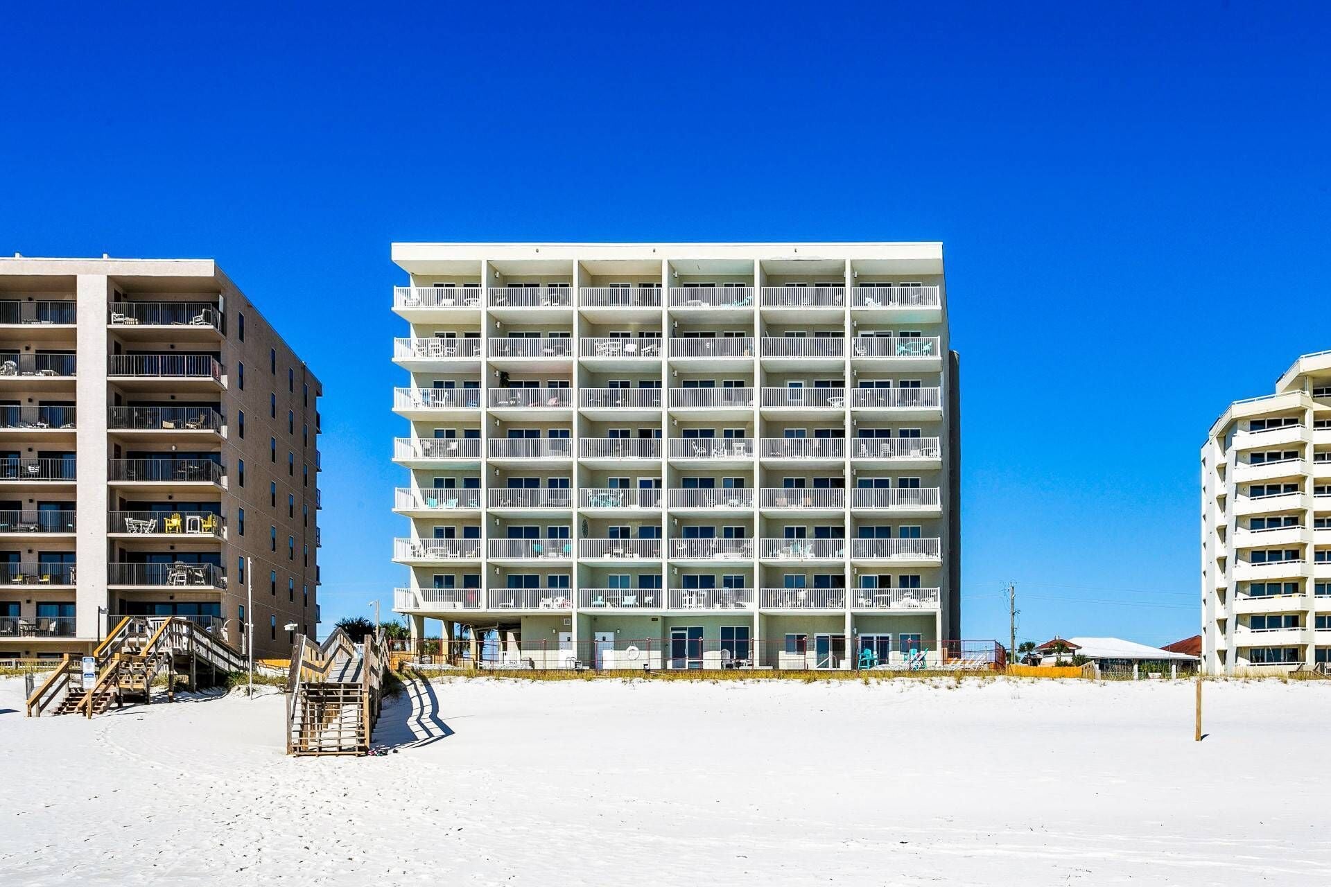 A multi-story hotel with balconies, located on a beach.