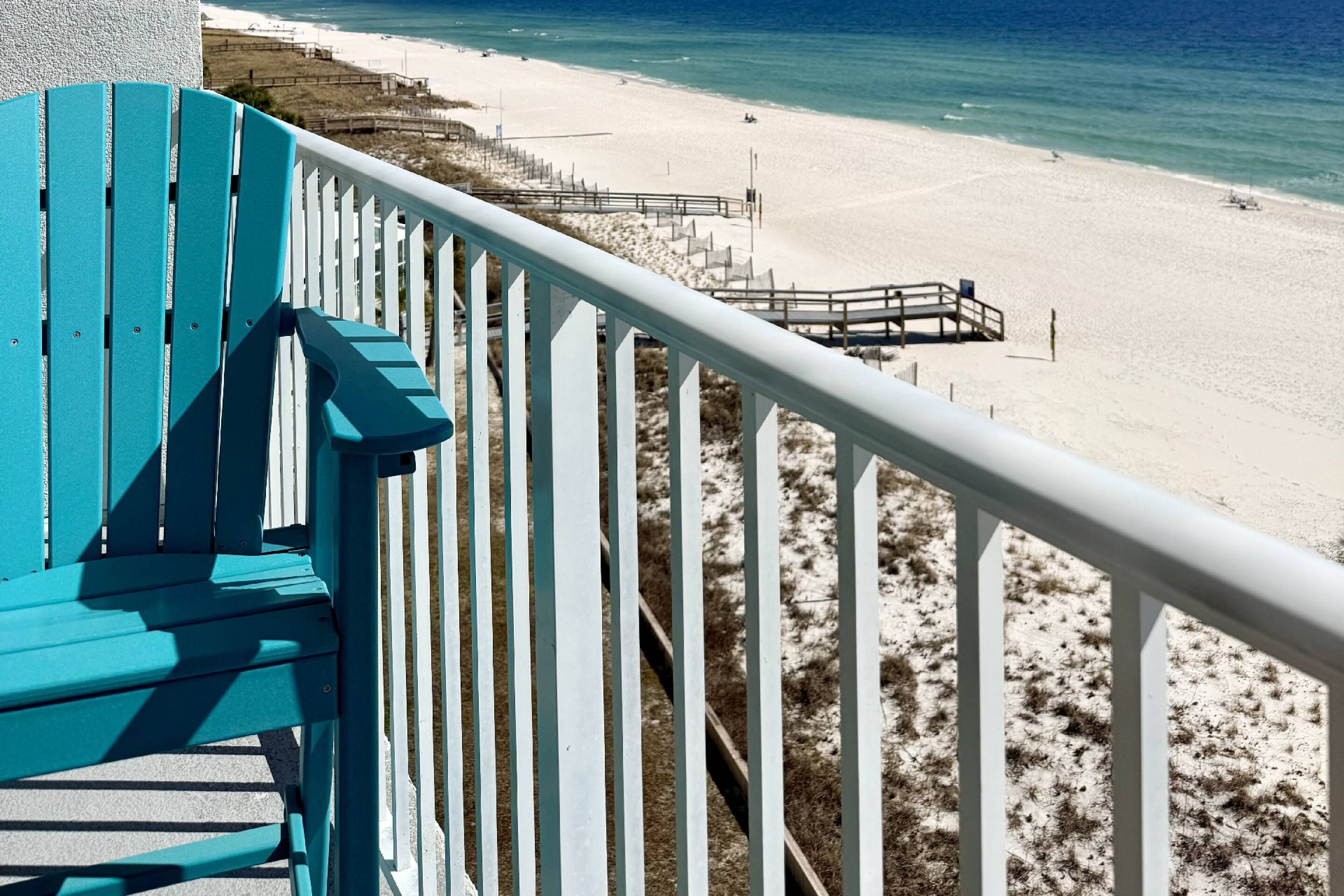 Une chaise turquoise et une rambarde blanche surplombent une plage, avec une promenade en bois.