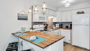 A modern kitchen with white cabinets, a wooden island, pendant lights, and a refrigerator. - Perdido Skye Beach Front Condo | King Bed/Bunk Quarters | Gulf Front Views | Private Balcony | Pool (Pensacola)