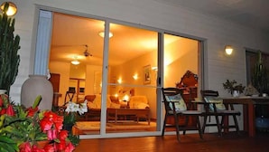 Una habitación con puerta corrediza de vidrio que da a un espacio exterior, un sofá, una silla y una mesa con un florero y plantas.