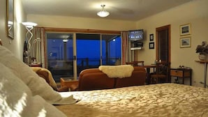 Habitación de hotel con cama, escritorio, silla, televisor y balcón con vistas.
