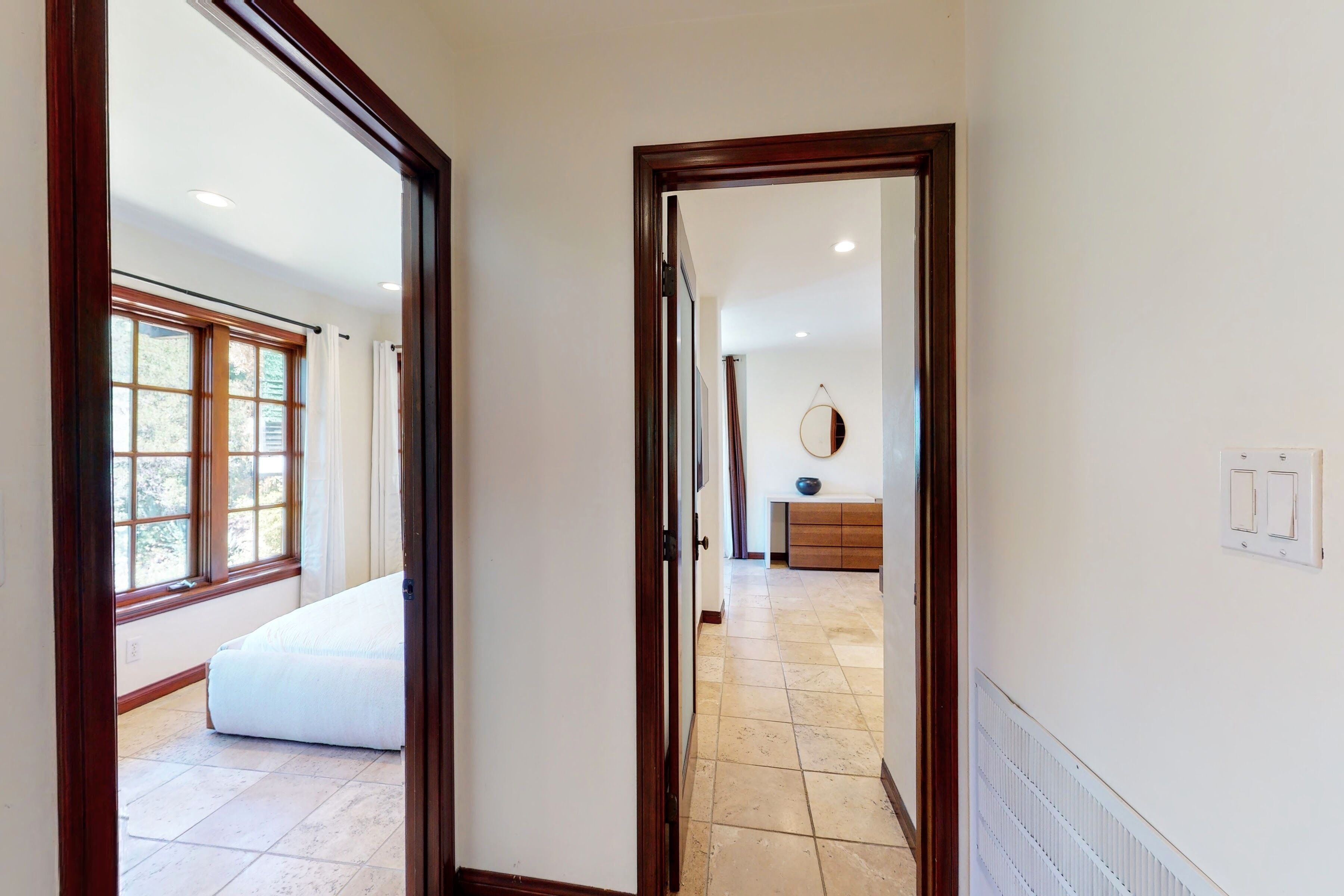 A hallway with a bed, a dresser, and a mirror.