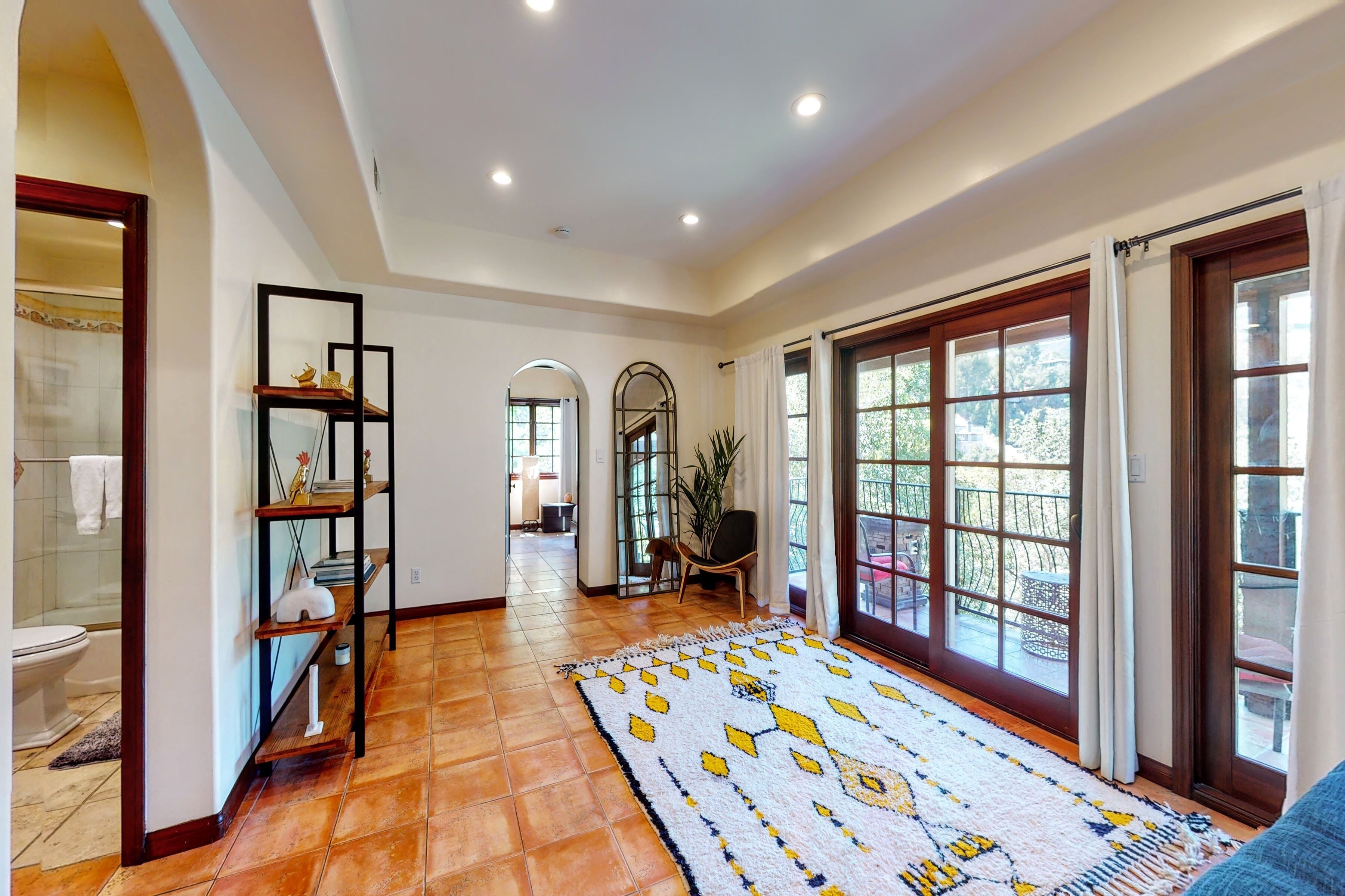 A spacious hallway with a patterned rug, wooden shelves, and large windows with curtains.