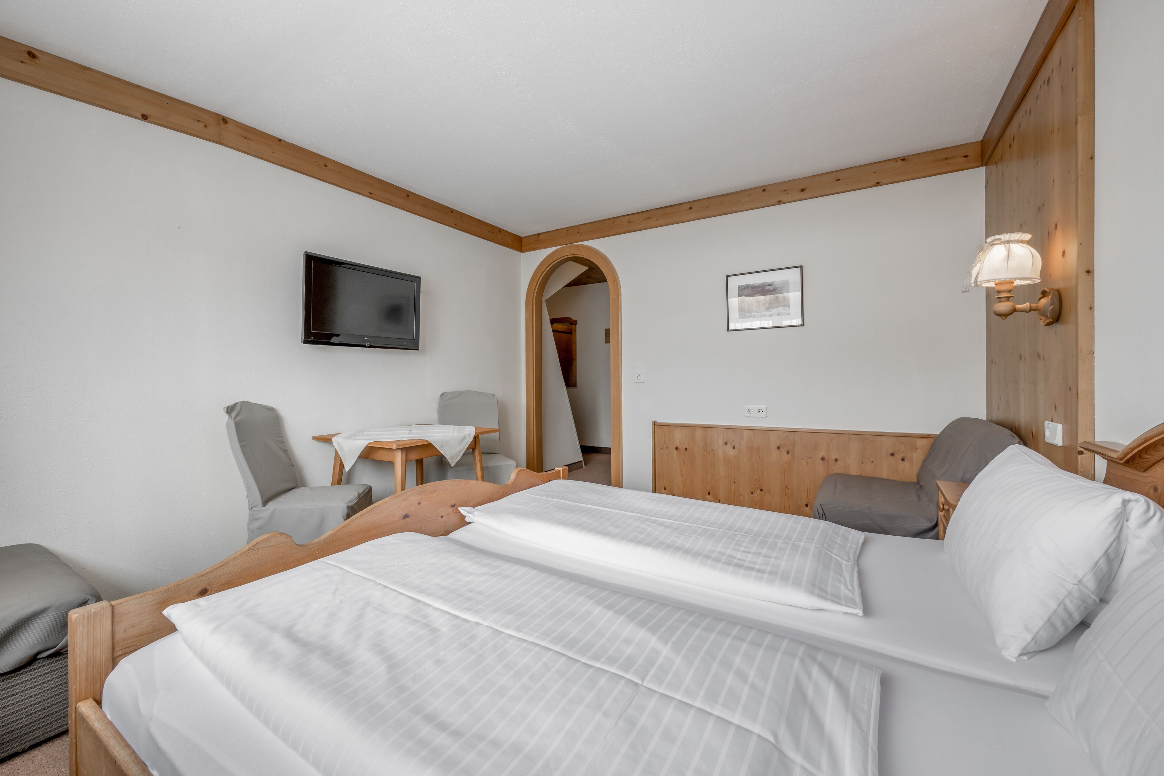Une chambre d’hôtel avec un lit en bois, un téléviseur fixé au mur, un bureau avec une chaise et un plafond en bois.