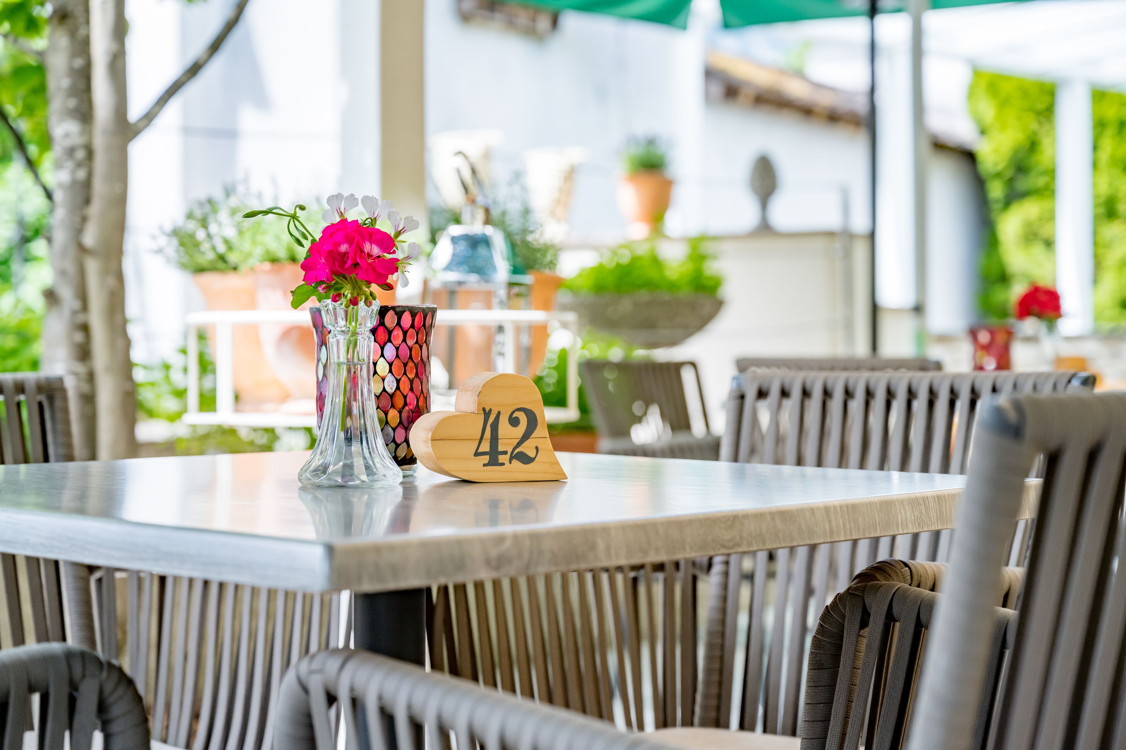 A dining table with a number 42 sign, a vase with flowers, and wicker chairs.