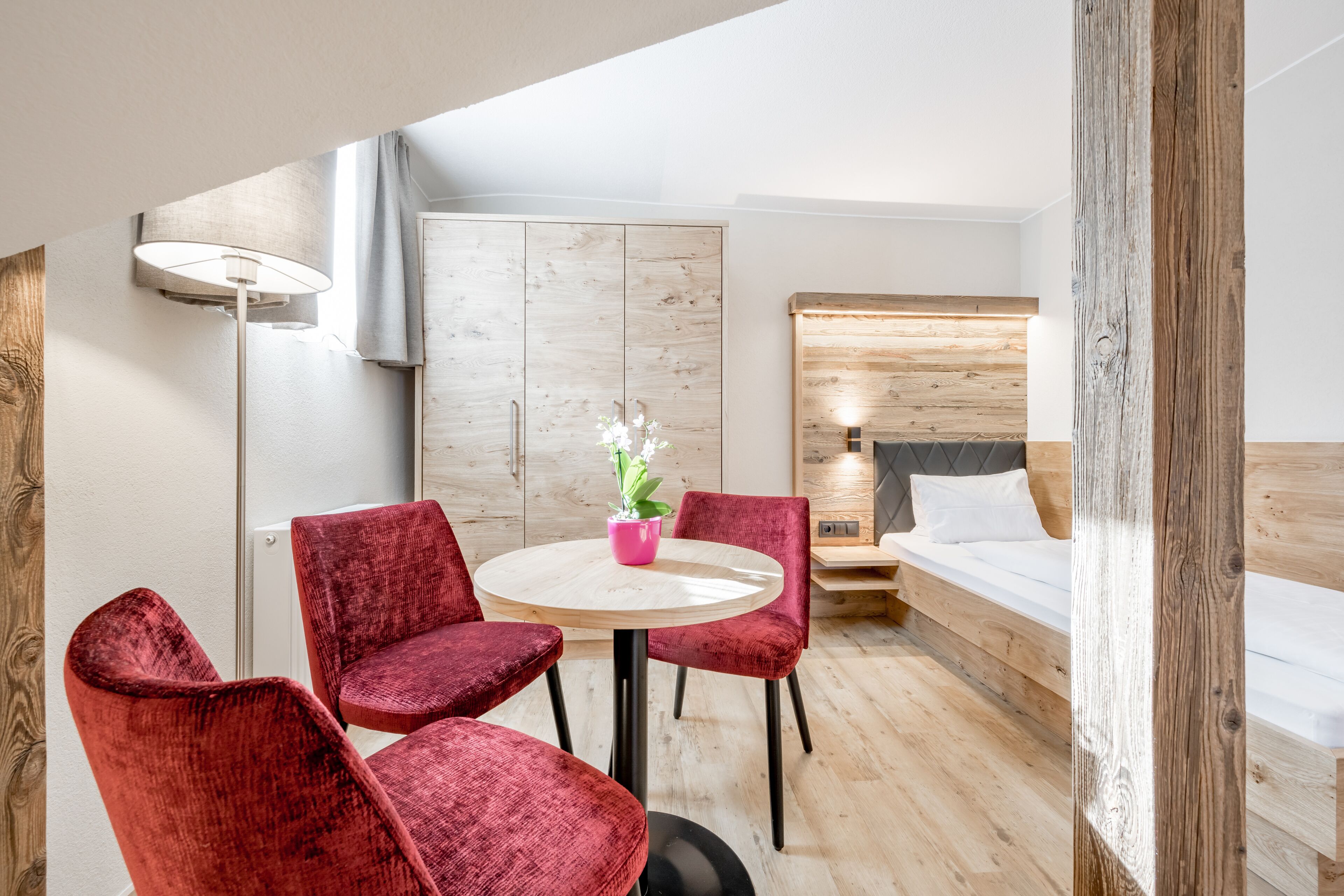 Een moderne hotelkamer met een houten vloer, een ronde tafel met stoelen, een bed met houten hoofdeinde en een kastje met een licht houten afwerking.