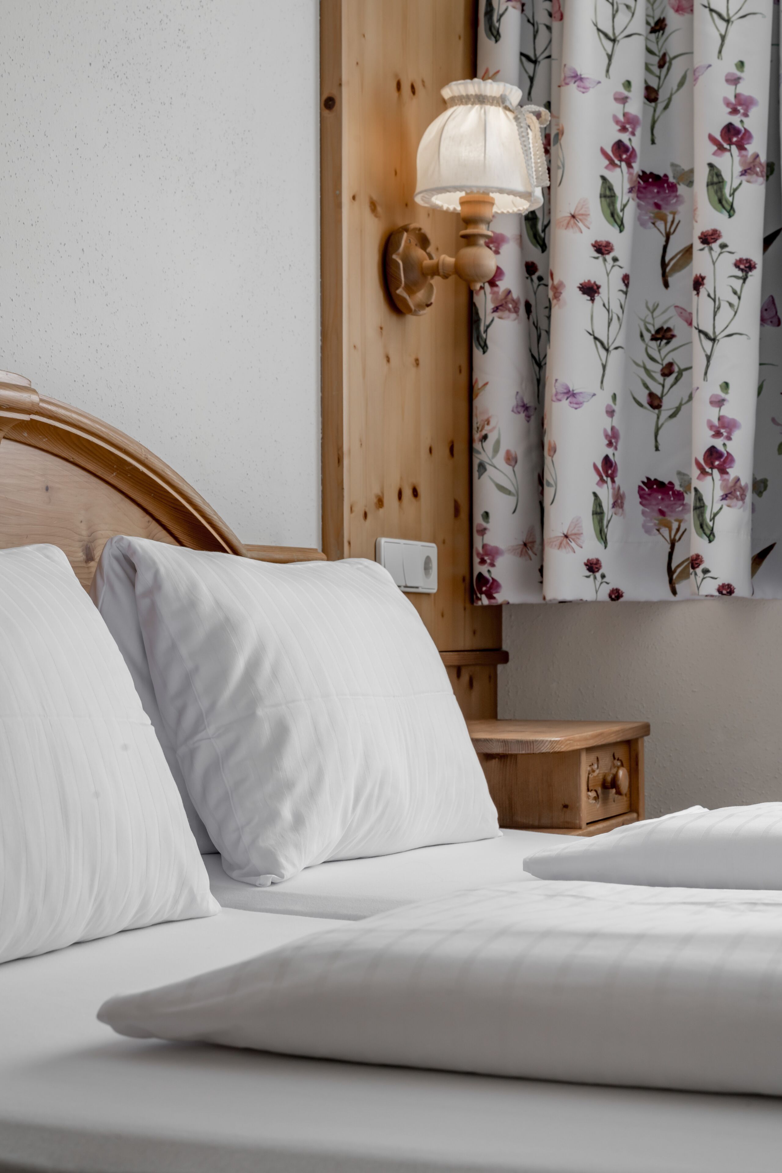A neatly made bed with white linens, a wooden headboard, and a wall-mounted lamp.