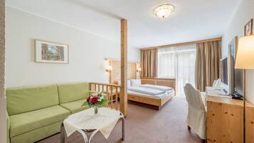 Ein Hotelzimmer mit einem grünen Sofa, einem kleinen Tisch mit Blumenvase, einem Bett mit Holz Kopfteil, einem Schreibtisch mit Computer und einem Fernseher.