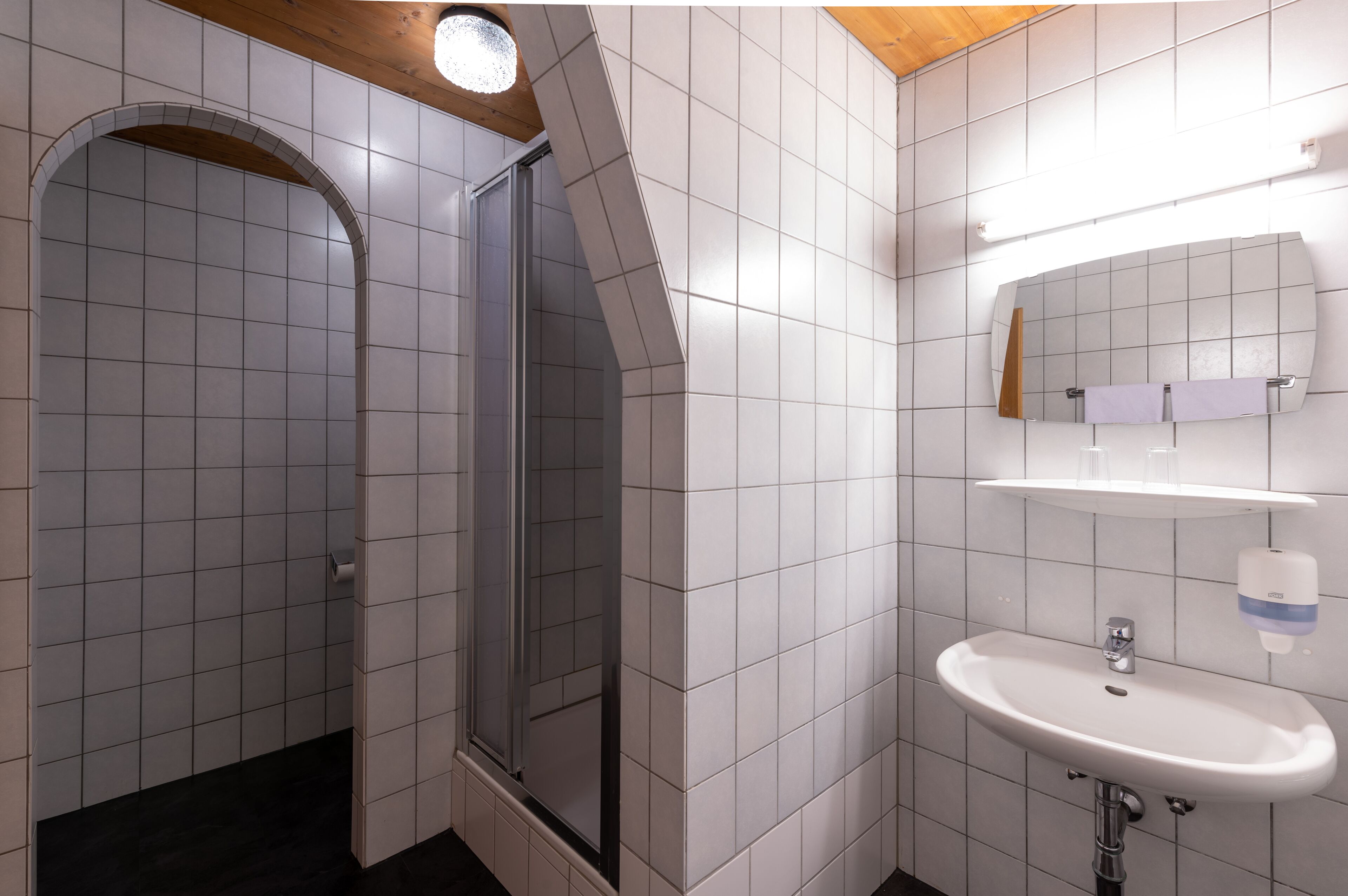 A modern bathroom with white tiles, a glass shower enclosure, a sink with a mirror, and a towel rack.