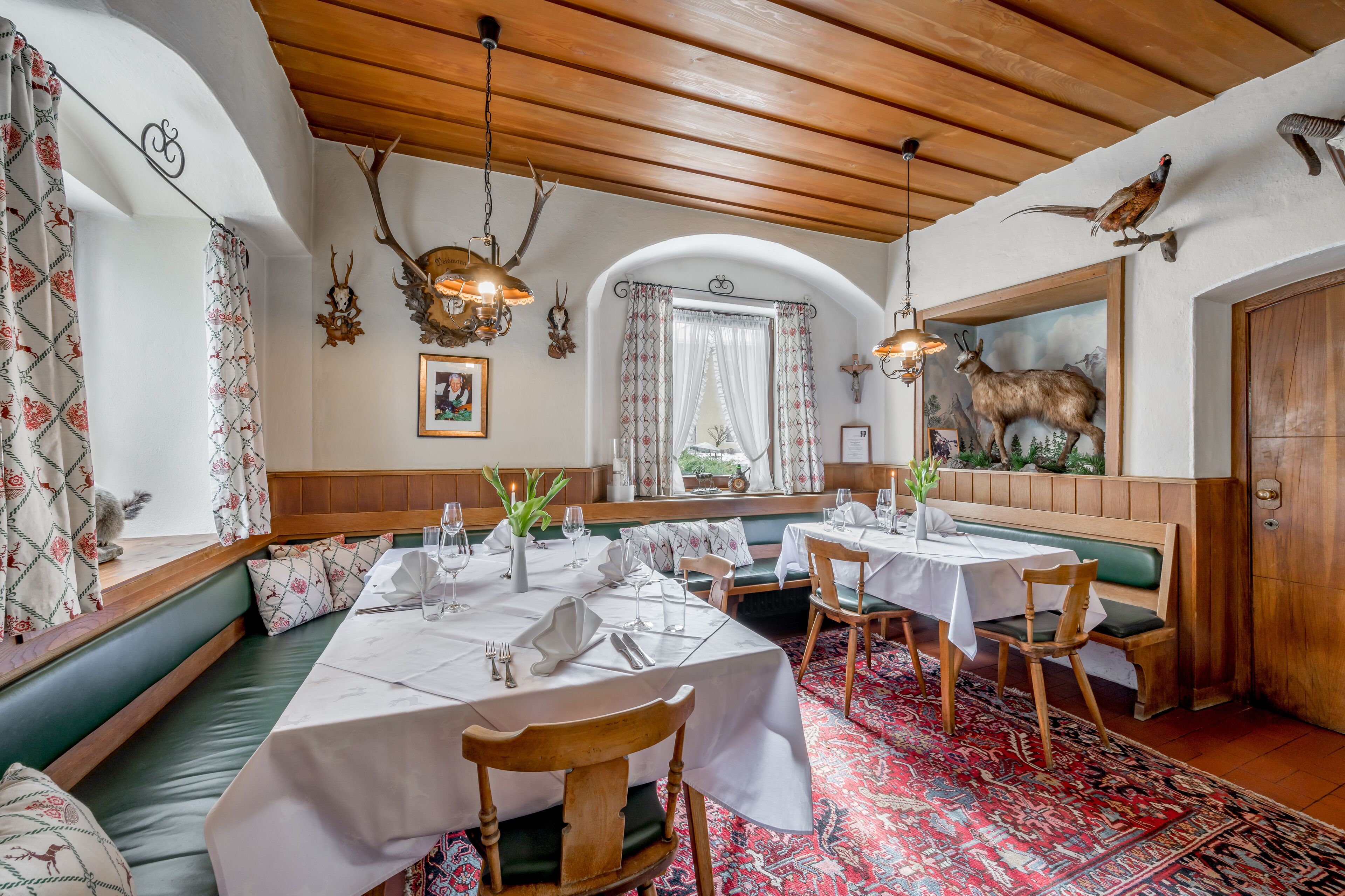 Un espace repas avec des bancs en bois, des nappes blanches et un tapis à motifs.