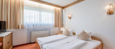A hotel room with two beds, a wooden headboard, a TV, a radiator, and a window with curtains.